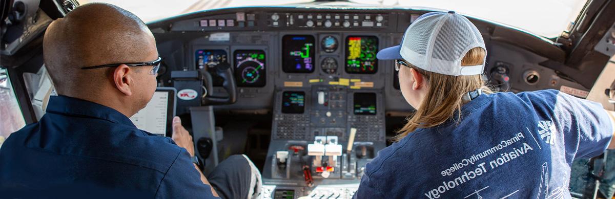两名航空专业的学生坐在一架商用飞机的驾驶舱里操作控制系统